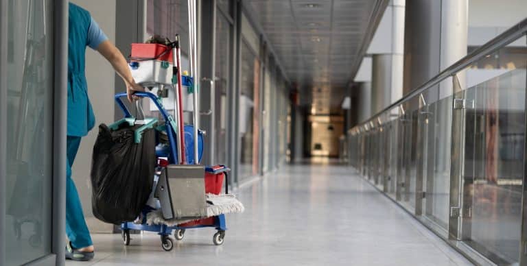 Schoonmaker met trolley in een lange kantoorgang