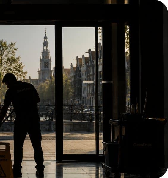 CleanOnes-medewerker dweilt de entree van een Amsterdams kantoor met zicht op de grachten en de Zuiderkerk